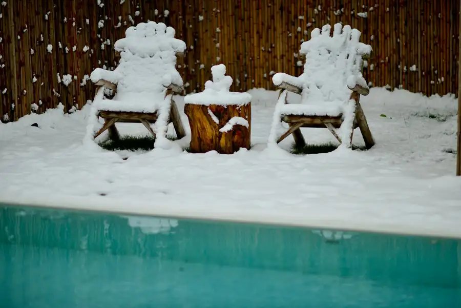 Snow-covered Muskoka chairs beside a pool edge in early winter